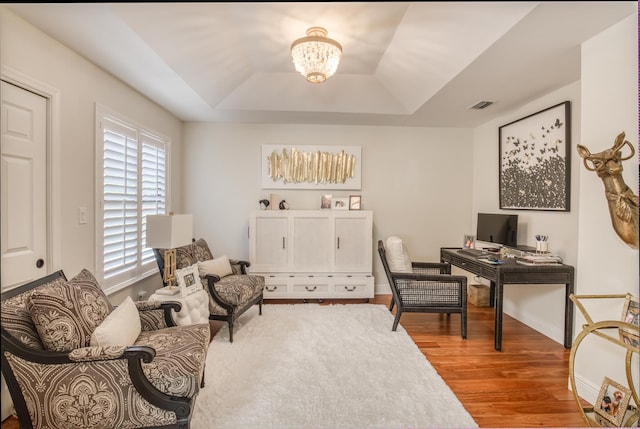 office space with a raised ceiling, hardwood / wood-style floors, and a notable chandelier