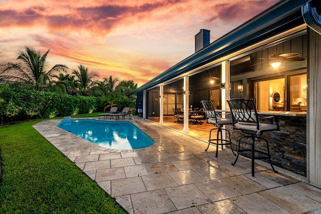 pool at dusk featuring a patio area and a yard