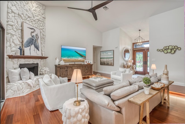 living room with hardwood / wood-style floors, ceiling fan with notable chandelier, a fireplace, and high vaulted ceiling