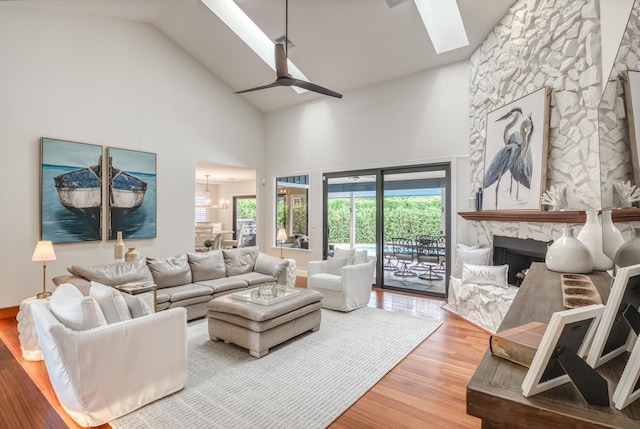 living room with ceiling fan with notable chandelier, high vaulted ceiling, hardwood / wood-style flooring, and a stone fireplace