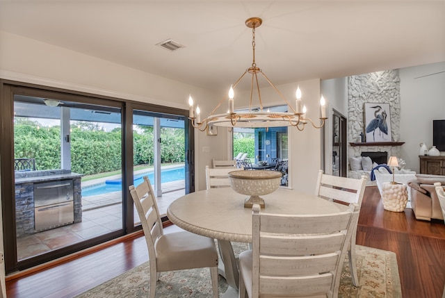 dining space with hardwood / wood-style floors, a stone fireplace, and an inviting chandelier