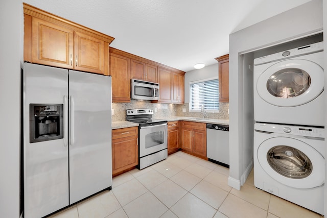 kitchen featuring appliances with stainless steel finishes, tasteful backsplash, sink, light tile patterned floors, and stacked washer / drying machine