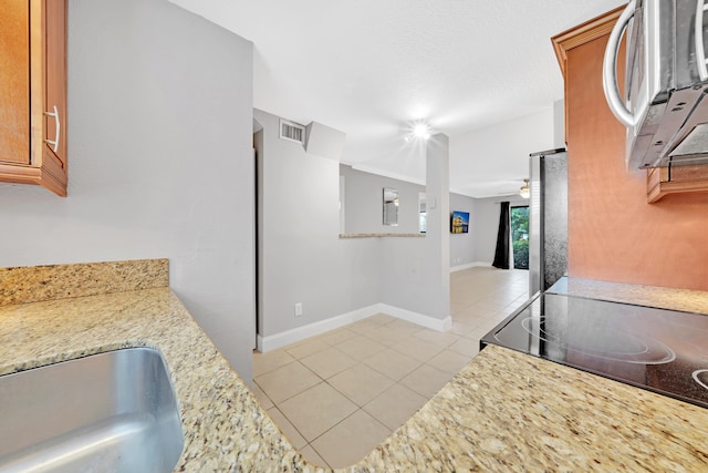 kitchen featuring ceiling fan, light tile patterned floors, stainless steel refrigerator, and light stone counters