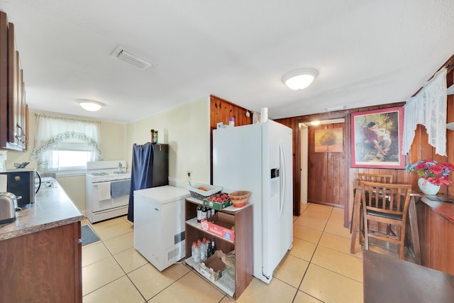 kitchen with light tile patterned floors, visible vents, white appliances, and wooden walls