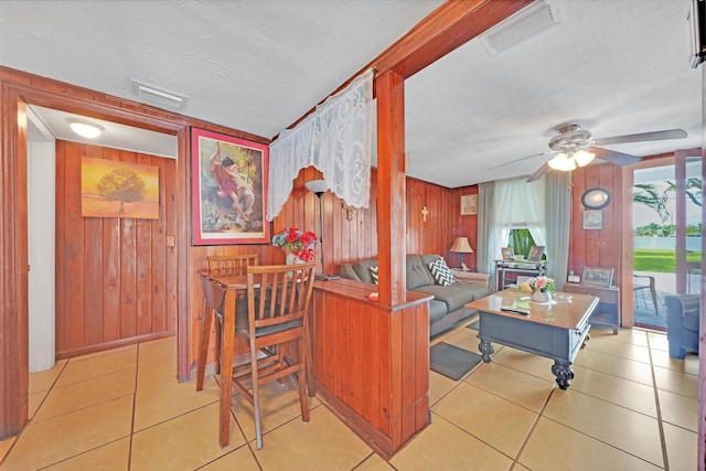 tiled living area featuring visible vents, wood walls, a textured ceiling, and ceiling fan