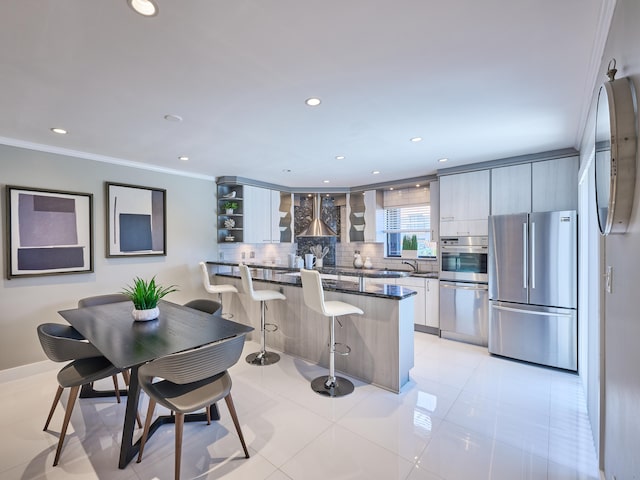 kitchen with appliances with stainless steel finishes, a kitchen breakfast bar, decorative backsplash, light tile patterned flooring, and crown molding