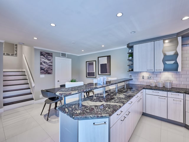 kitchen with kitchen peninsula, light tile patterned floors, dark stone counters, crown molding, and decorative backsplash