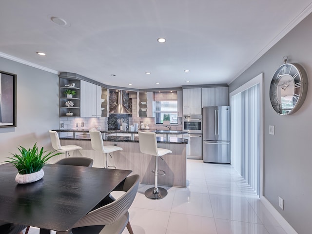 kitchen with stainless steel appliances, tasteful backsplash, light tile patterned floors, crown molding, and wall chimney exhaust hood