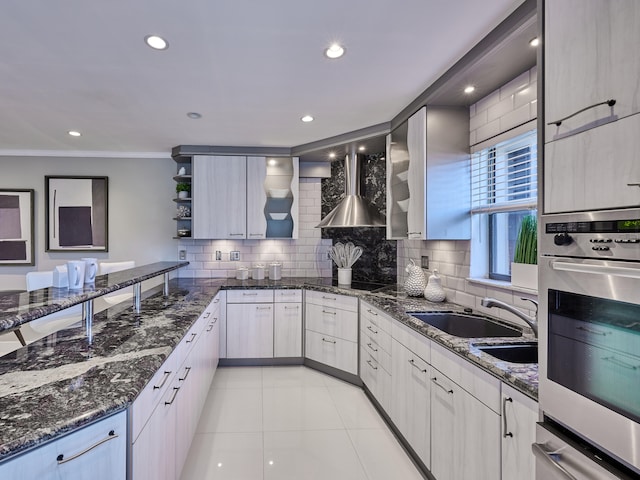 kitchen featuring wall chimney range hood, dark stone countertops, oven, and tasteful backsplash