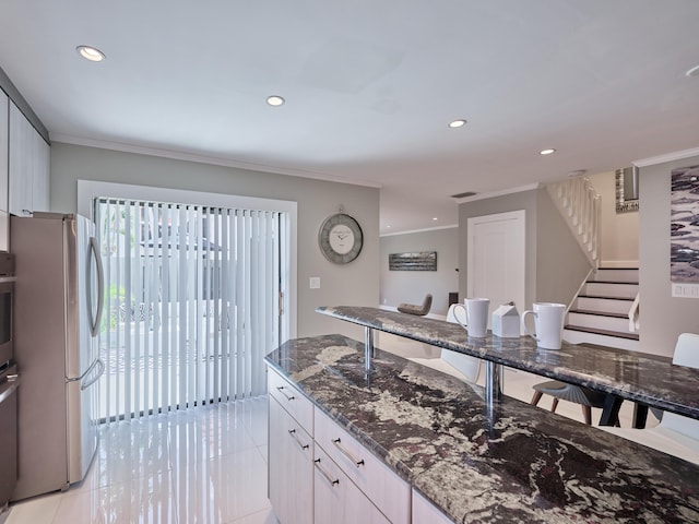 kitchen with a breakfast bar area, stainless steel fridge, ornamental molding, dark stone counters, and light tile patterned flooring