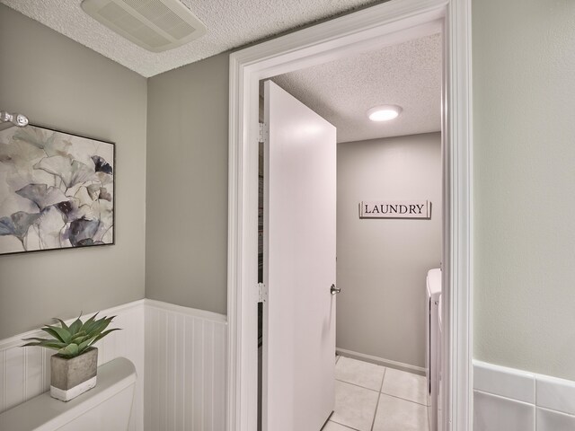 hallway featuring a textured ceiling, separate washer and dryer, and light tile patterned flooring