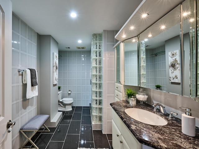 bathroom with toilet, tile patterned floors, tile walls, vanity, and a shower