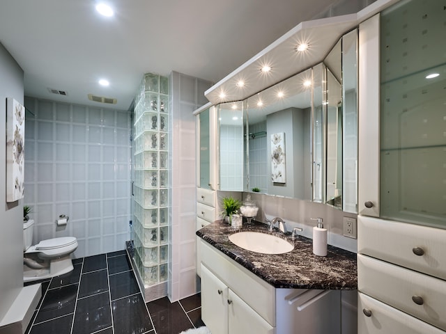 bathroom with a shower with door, tile walls, toilet, vanity, and tile patterned flooring