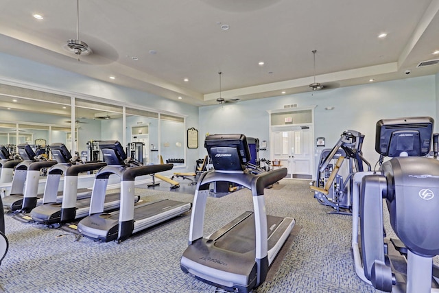 exercise room with ceiling fan, carpet floors, and a raised ceiling