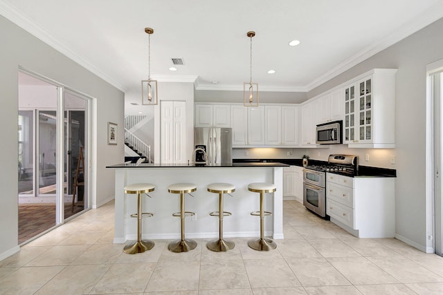 kitchen featuring a kitchen island with sink, white cabinets, a kitchen bar, stainless steel appliances, and crown molding