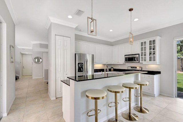 kitchen featuring a breakfast bar, a kitchen island with sink, white cabinets, appliances with stainless steel finishes, and ornamental molding