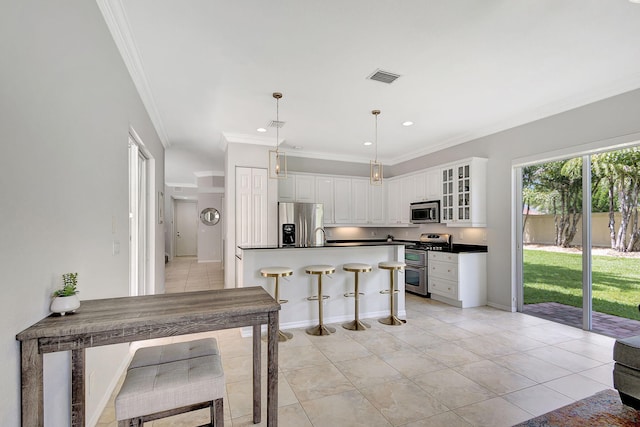 kitchen featuring white cabinets, hanging light fixtures, appliances with stainless steel finishes, crown molding, and a kitchen bar