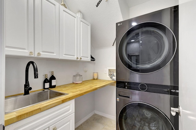 laundry room featuring cabinets, a textured ceiling, light tile patterned flooring, sink, and stacked washer and clothes dryer