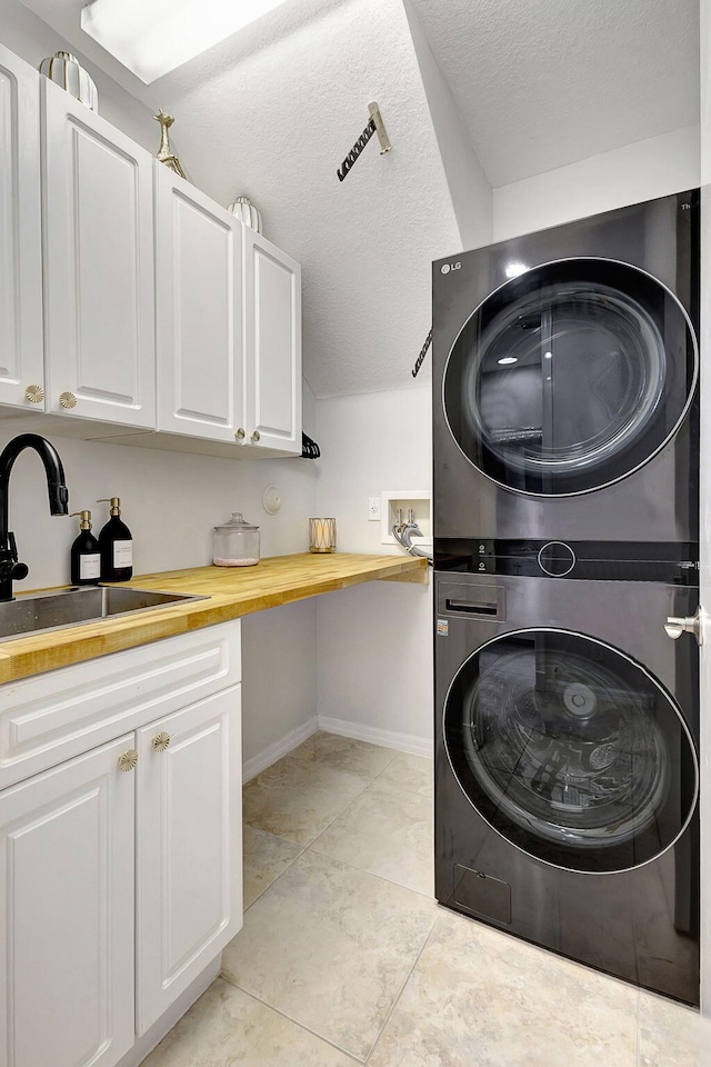 clothes washing area featuring light tile patterned floors, stacked washer / dryer, a textured ceiling, cabinets, and sink