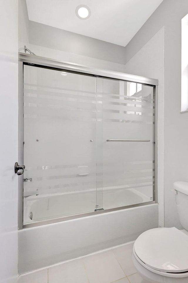 full bathroom featuring bath / shower combo with glass door, toilet, and tile patterned floors