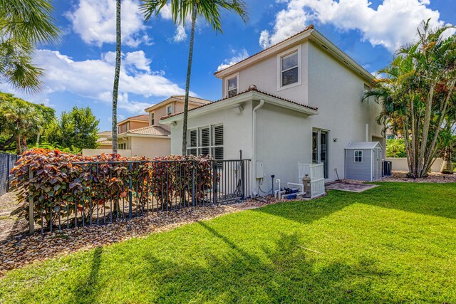 rear view of property featuring a storage shed, a yard, fence, and stucco siding