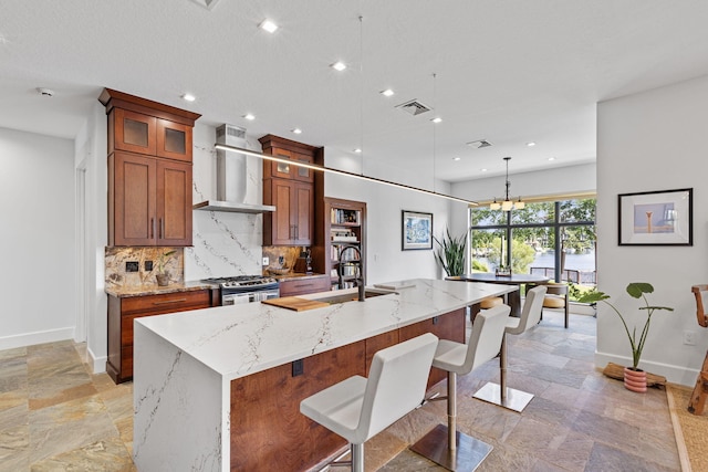 kitchen featuring a kitchen breakfast bar, decorative light fixtures, stainless steel stove, decorative backsplash, and wall chimney range hood