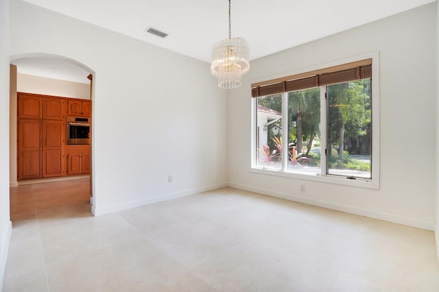 tiled spare room featuring plenty of natural light and a chandelier