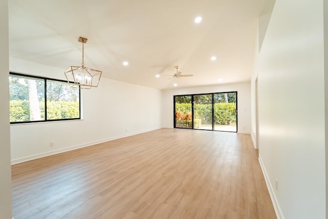 empty room with ceiling fan with notable chandelier and light hardwood / wood-style flooring