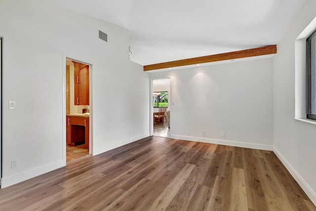 unfurnished room featuring lofted ceiling with beams, wood finished floors, visible vents, and baseboards