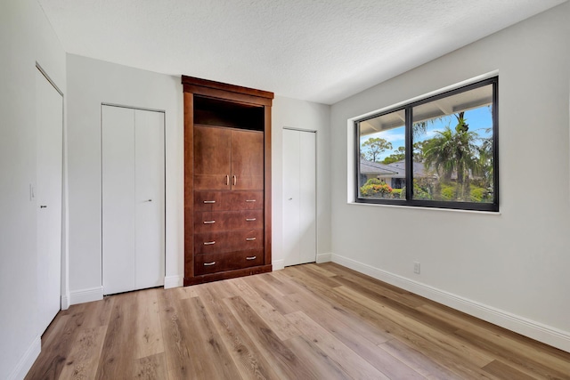 unfurnished bedroom with a textured ceiling, light hardwood / wood-style floors, and multiple closets