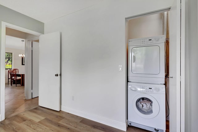 washroom with stacked washer and dryer, laundry area, light wood finished floors, baseboards, and a notable chandelier