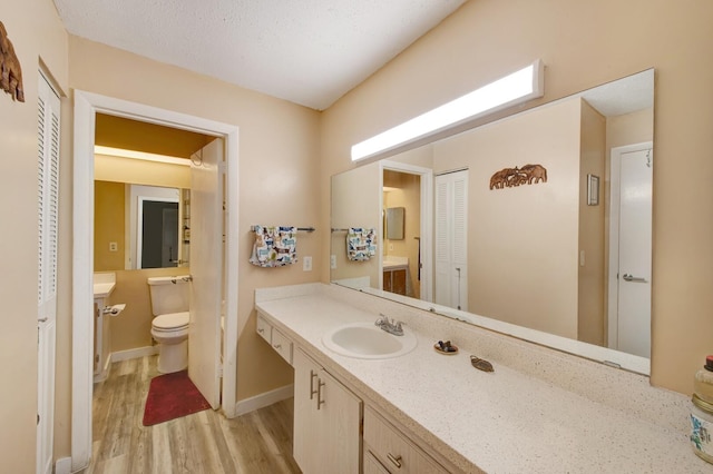 bathroom with wood-type flooring, a textured ceiling, vanity, and toilet