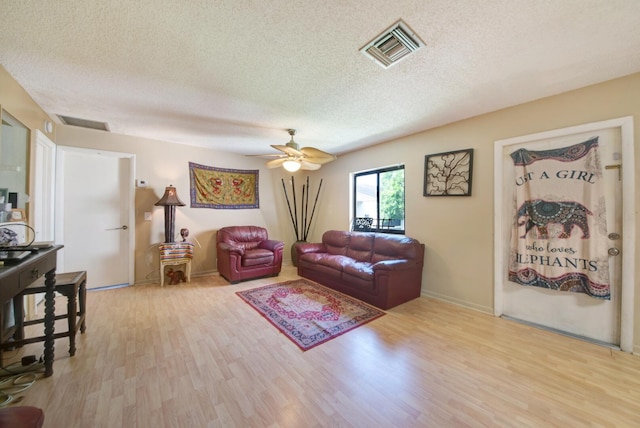 living room with ceiling fan, a textured ceiling, and light hardwood / wood-style floors