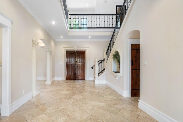 entrance foyer featuring arched walkways, decorative columns, baseboards, and stairs