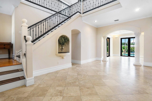 interior space with arched walkways, baseboards, a towering ceiling, ornamental molding, and ornate columns