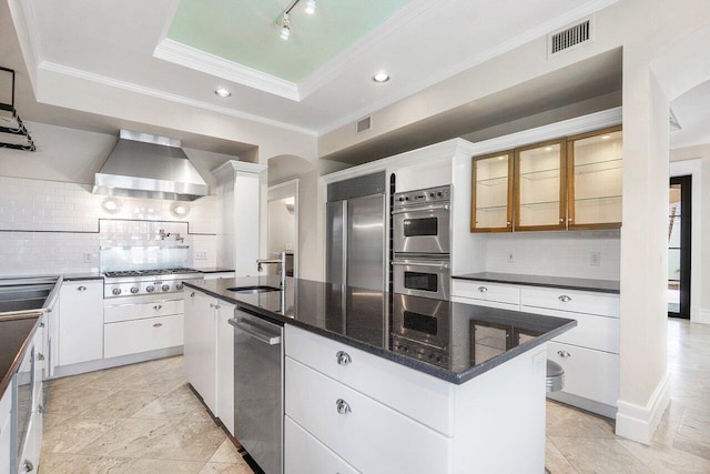 kitchen featuring visible vents, appliances with stainless steel finishes, a tray ceiling, wall chimney range hood, and a sink