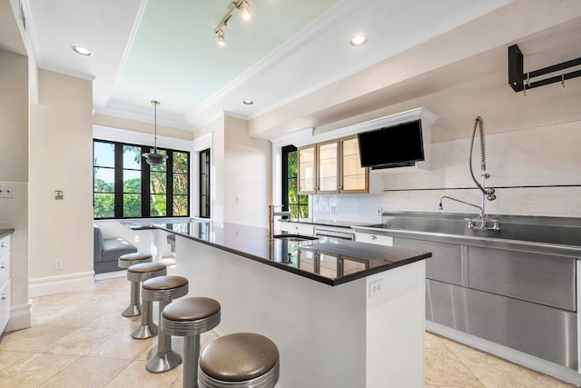 kitchen with decorative backsplash, dark countertops, a kitchen breakfast bar, crown molding, and a sink