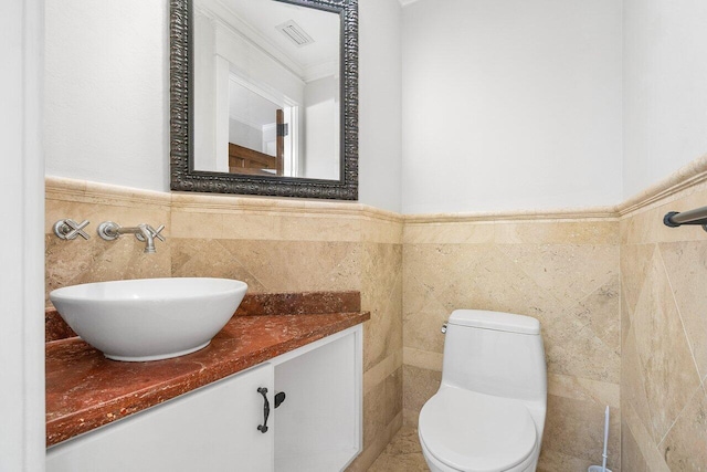 half bath featuring visible vents, toilet, a wainscoted wall, vanity, and tile walls