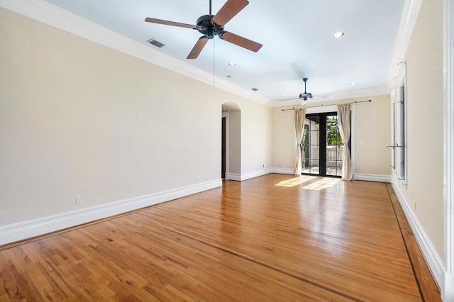 empty room with arched walkways, visible vents, light wood-style floors, baseboards, and crown molding