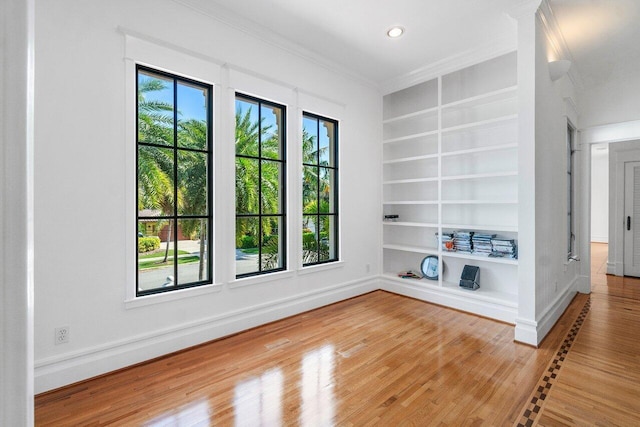 spare room with built in shelves, recessed lighting, wood finished floors, baseboards, and crown molding