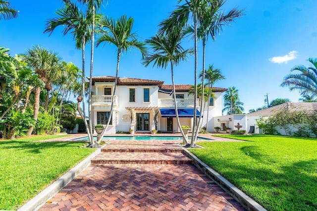 view of front of home featuring a balcony, stucco siding, an outdoor pool, and a front yard