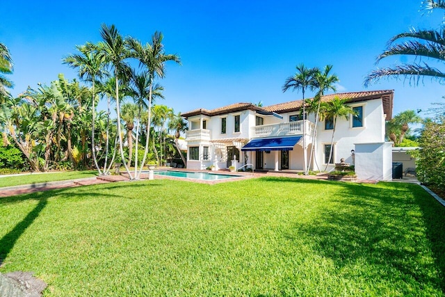 back of house with a balcony, stucco siding, an outdoor pool, and a yard