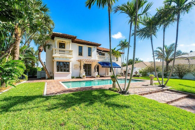 rear view of property featuring a balcony, an outdoor pool, a lawn, stucco siding, and a patio area