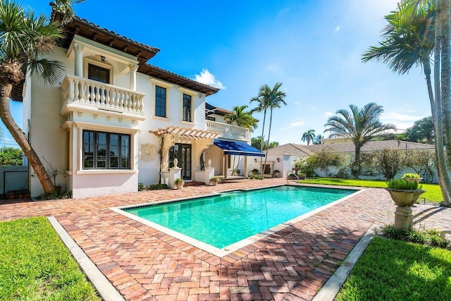 back of house featuring a balcony, a tiled roof, an outdoor pool, and stucco siding