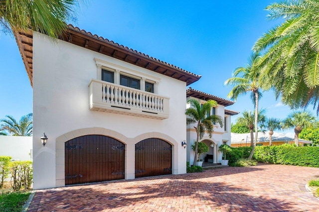 mediterranean / spanish house with a balcony, a tile roof, decorative driveway, a gate, and stucco siding