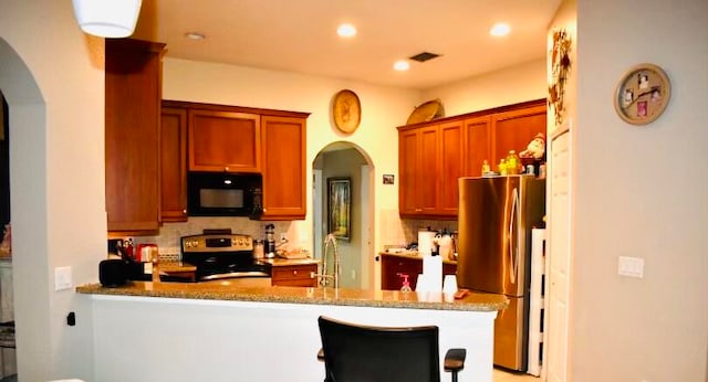 kitchen featuring appliances with stainless steel finishes, light stone counters, decorative backsplash, and kitchen peninsula