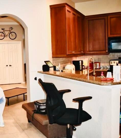 kitchen with kitchen peninsula, decorative backsplash, light tile patterned floors, and dark stone counters