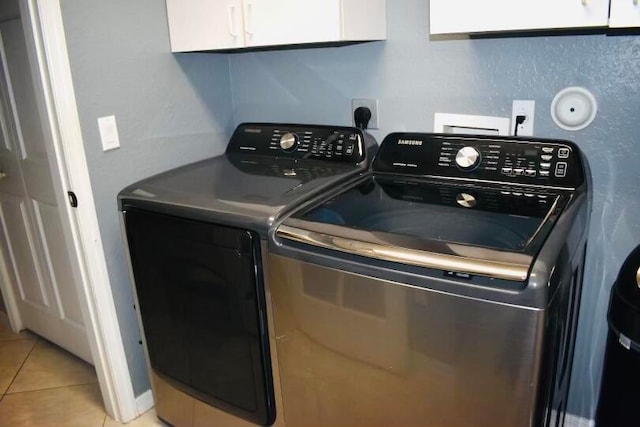 washroom with light tile patterned flooring, cabinets, and washing machine and clothes dryer