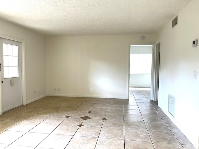 empty room featuring light tile patterned floors, plenty of natural light, and a textured ceiling