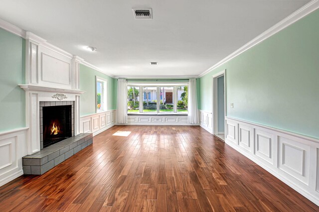 unfurnished living room with ornamental molding, a tiled fireplace, wood finished floors, and visible vents